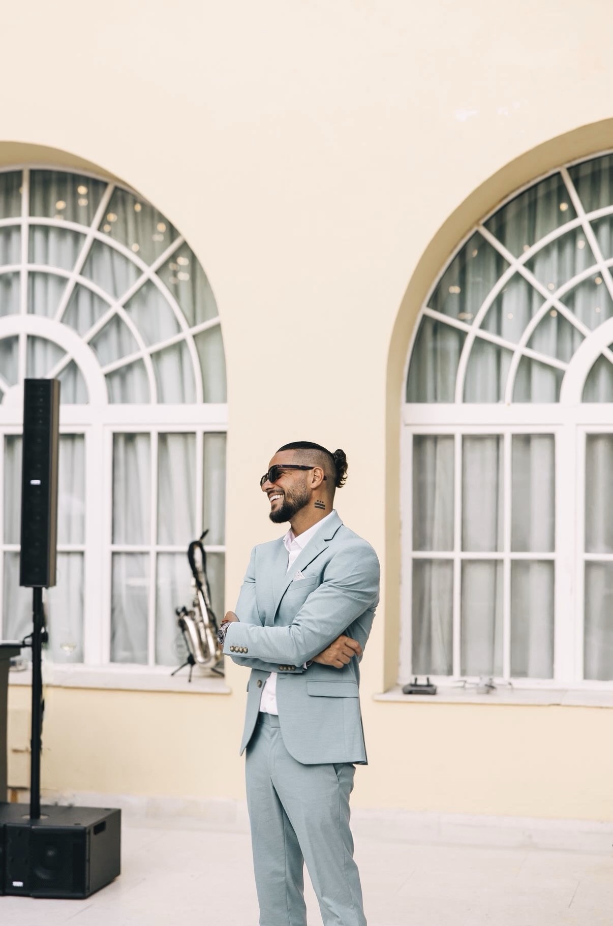 Luca Goya smiling in a light blue suit beside Mediterranean arched windows