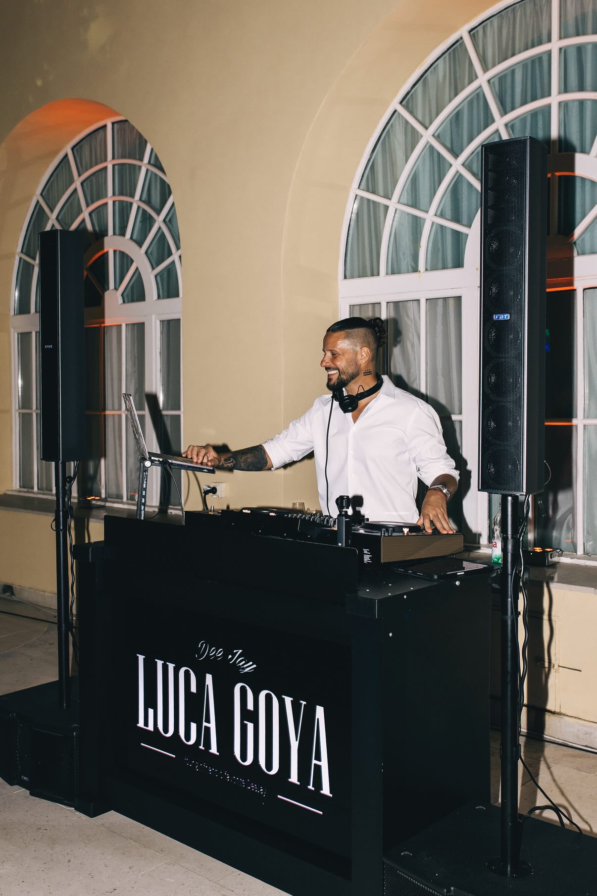 Luca DJing in a white shirt beneath arched windows